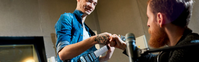 Two persons in a recording studio and one of them with a guitar